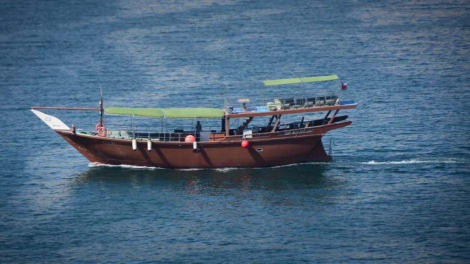 A traditional dhow boat sailing the clear waters of Musandam, Oman, under a bright day.