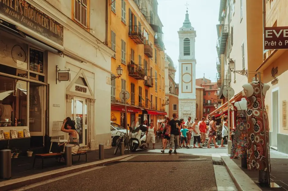 Bustling European street scene with tourists, shops, and a picturesque church tower.