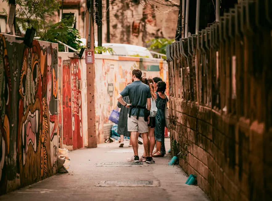 Group explores vibrant street art in a colorful Bangkok alleyway.